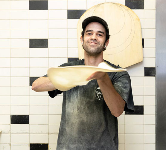 Mig's pizza maker in back stretching/tossing dough.